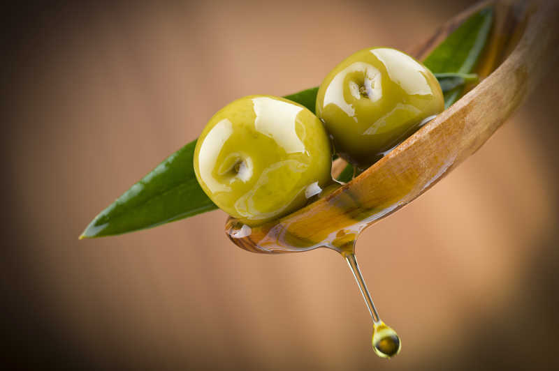 木色背景下木汤匙上的两个橄榄滴落的橄榄油