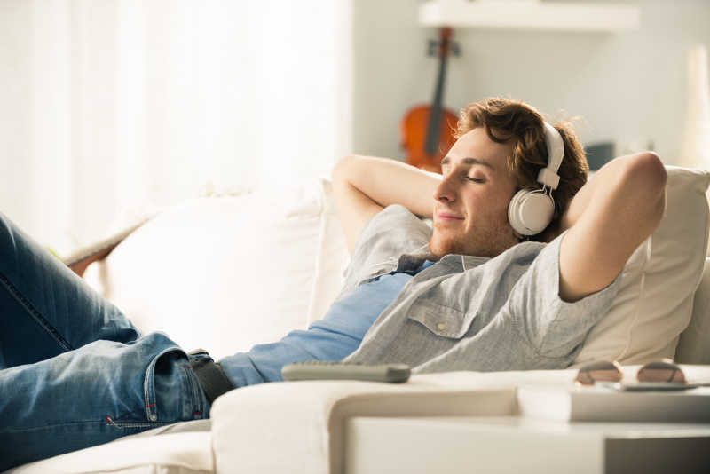 躺在白色沙发上戴着耳机听音乐的年轻人