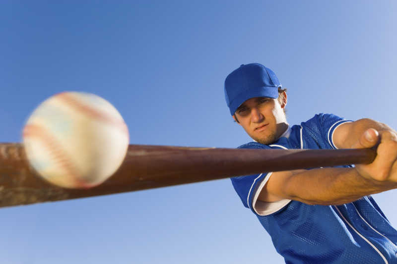 棒球运动员在晴朗的蓝天下用球棒击打球