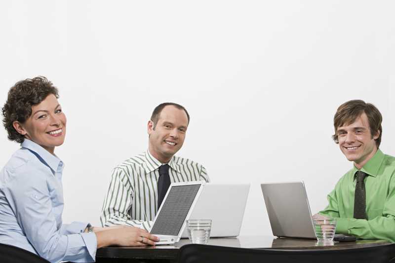 办公桌电脑旁微笑的三个商人