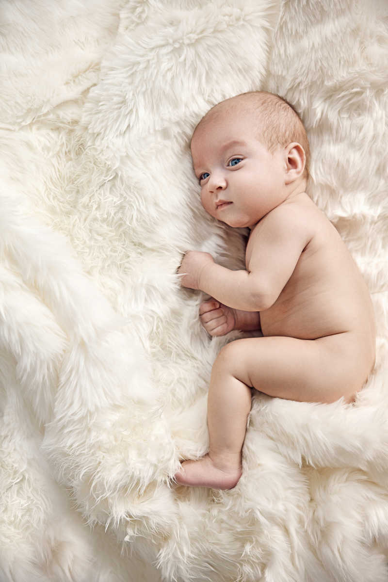 新生儿躺在白色毯子上