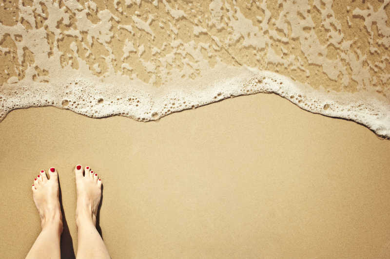 涂着红指甲的脚站在海滩上