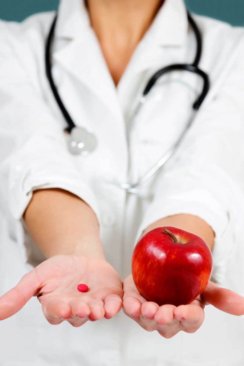 一手拿着药丸一手拿着苹果的女医生