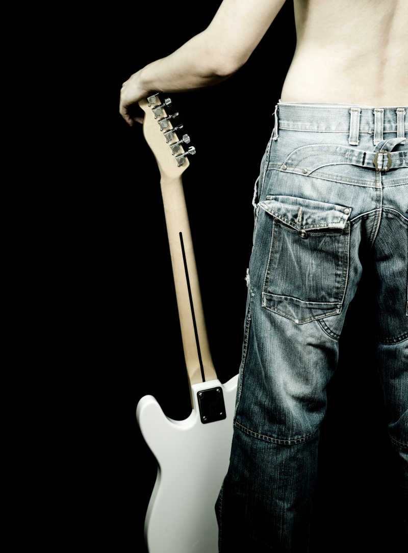 黑色背景上穿着牛仔裤的男人拿着吉他