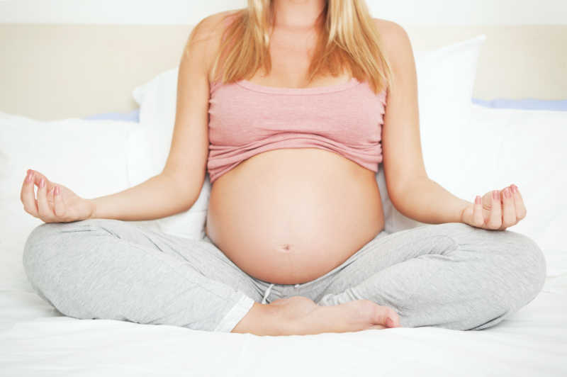 一位年轻的孕妇在卧室里做瑜伽冥想