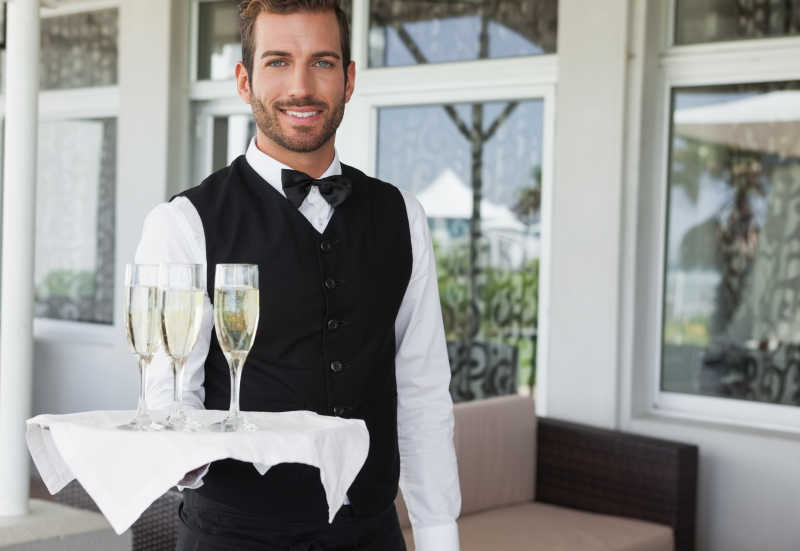 英俊微笑的服务员拿着香槟盘