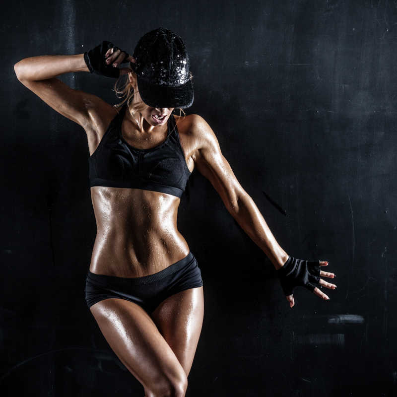 黑色背景下穿着运动背心摆舞蹈姿势的健身女性