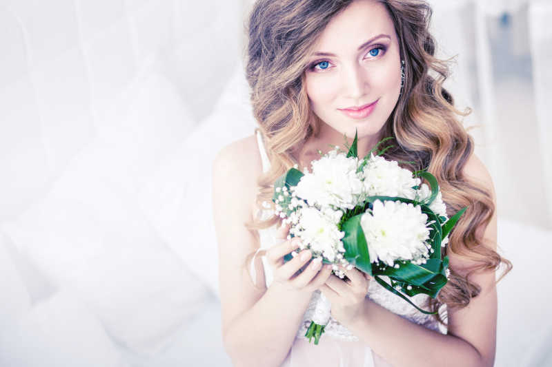 白色背景下拿着白色花的美丽新娘