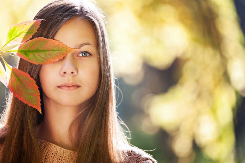 阳光背景下的拿着树叶挡着脸的女孩