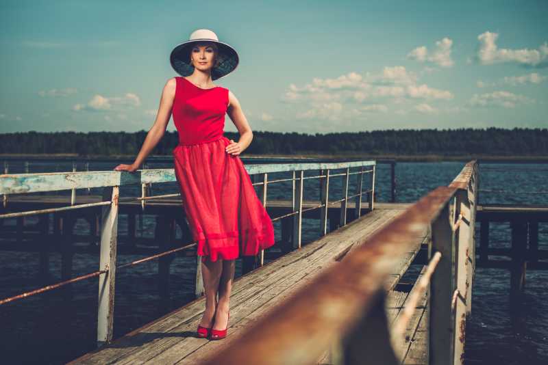 戴着白色帽子和红色衣服的时髦女人站在老木头码头上