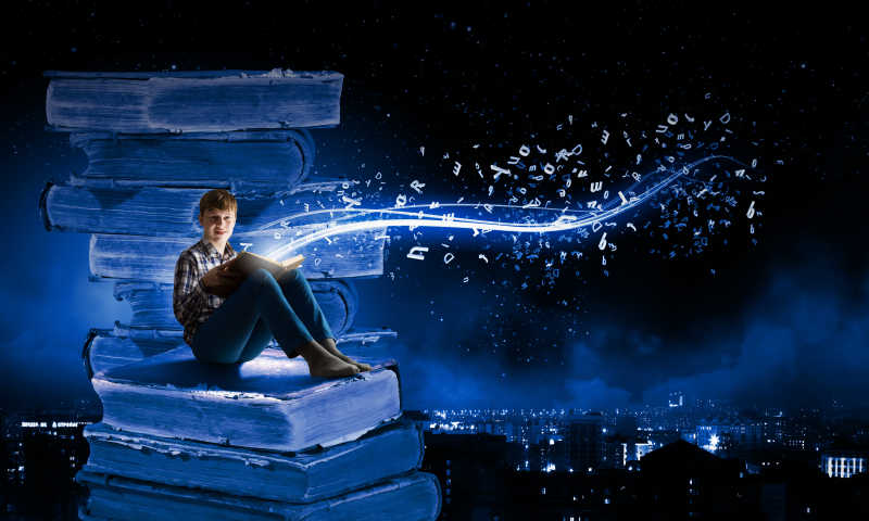 坐在厚厚的书籍上看书的小男孩