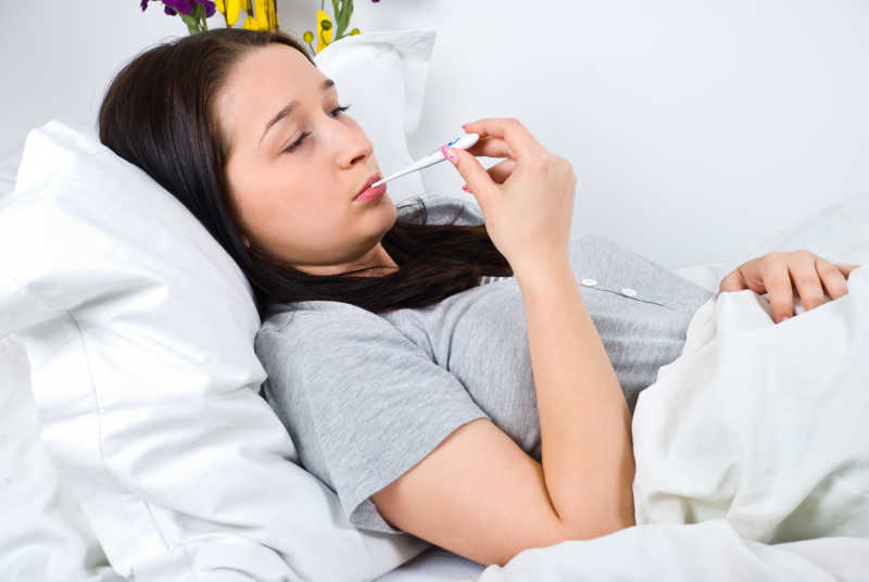 生病的年轻女子躺在床上用体温计检查体温