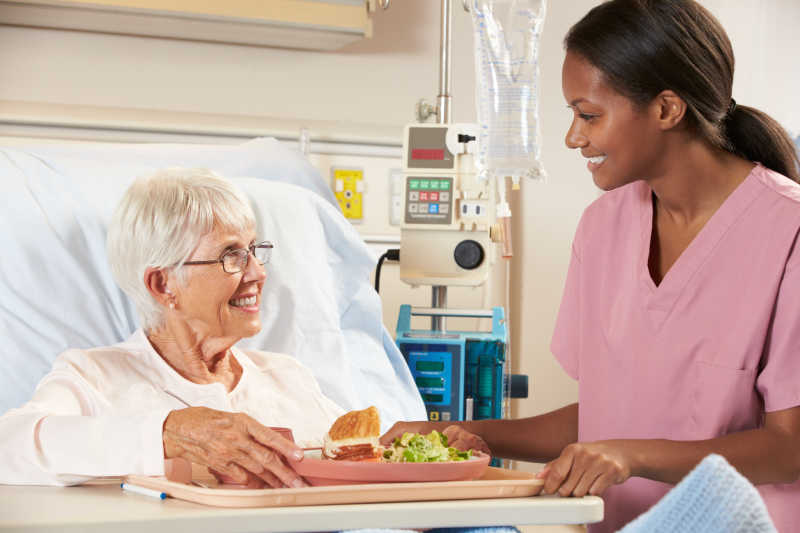 护士在病床边帮助老年女性病人吃早餐