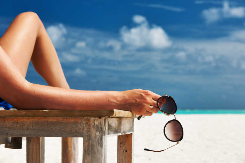 海滩放松的女人手里拿着太阳镜