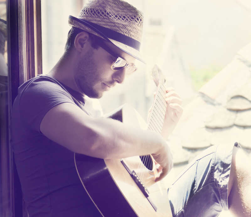 坐在窗边弹吉他的年轻人