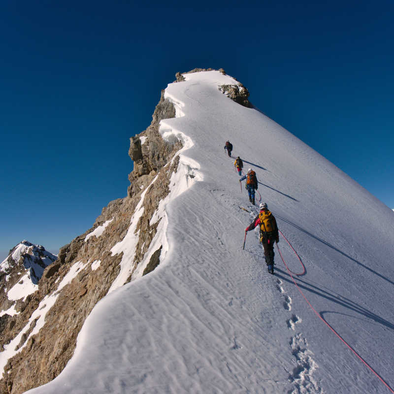 沿着一根绳子即将攀登顶峰的登山者