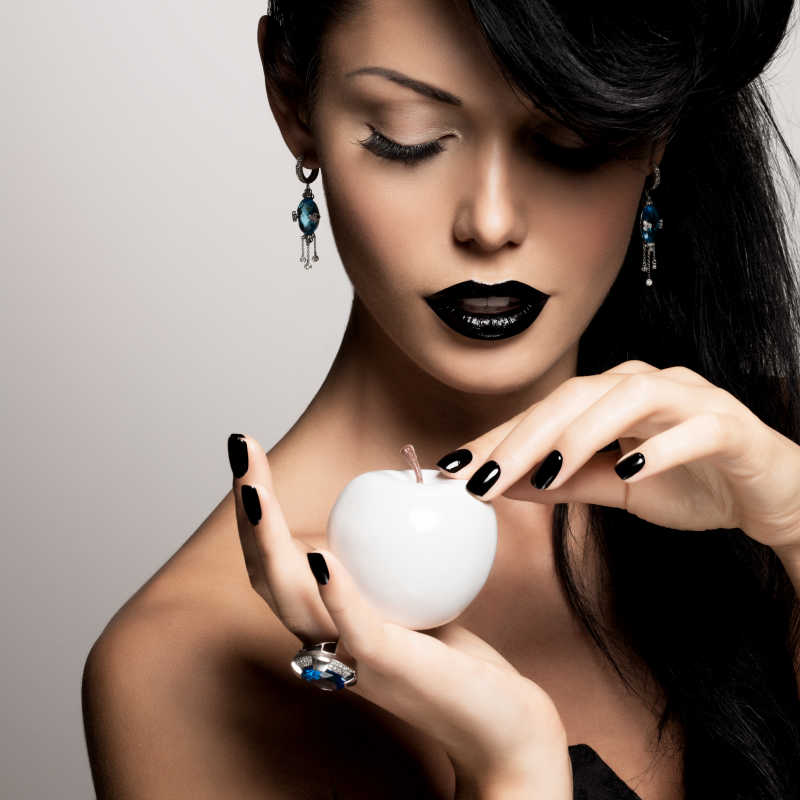带有黑色指甲和风格化妆的时尚模特抓住了白苹果