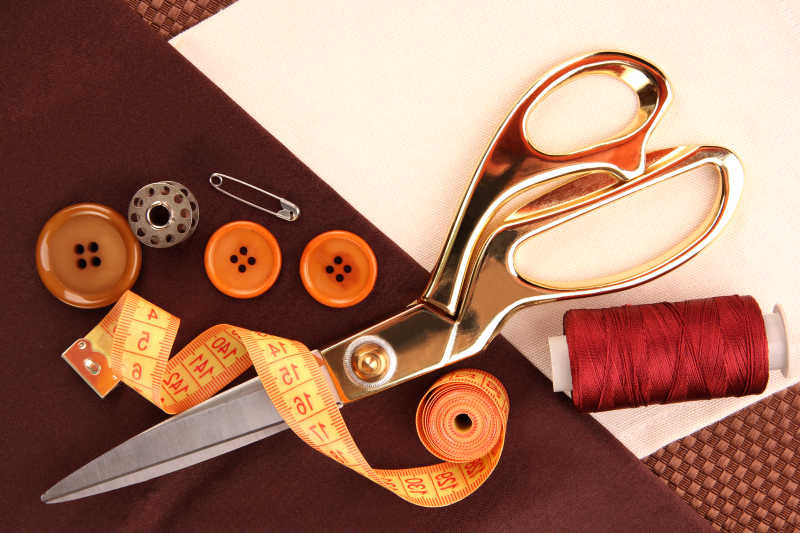 棕色和白色交织的背景下的剪刀纽扣皮尺等缝纫工具
