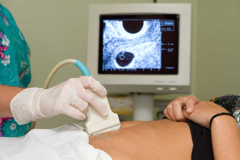 医生持有超声诊断医疗设备在孕妇肚子上探测扫描