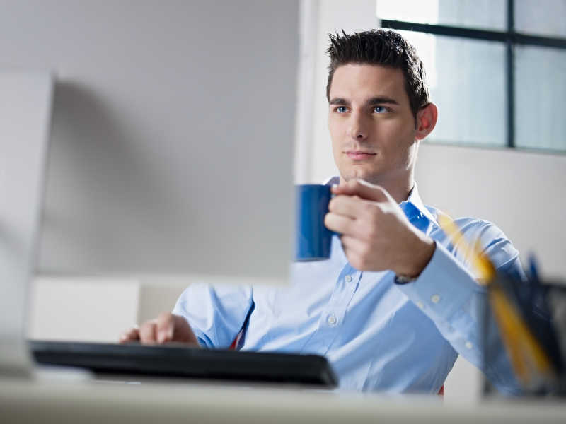 一个成年白人男性商人盯着电脑屏幕拿着蓝色咖啡杯