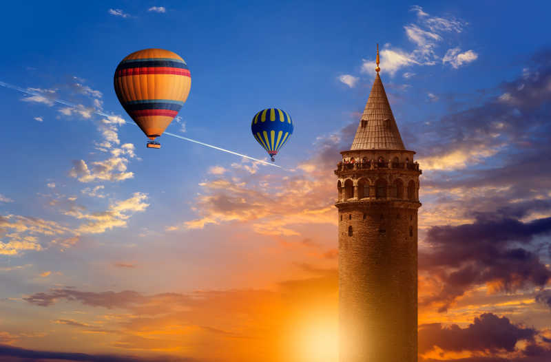 蓝天白云阳光下的Galata塔旁边的彩色的热气球