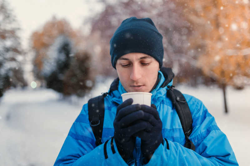 一名男子身穿明亮的蓝色冬季运动夹克和手持热饮料一次性外卖纸杯