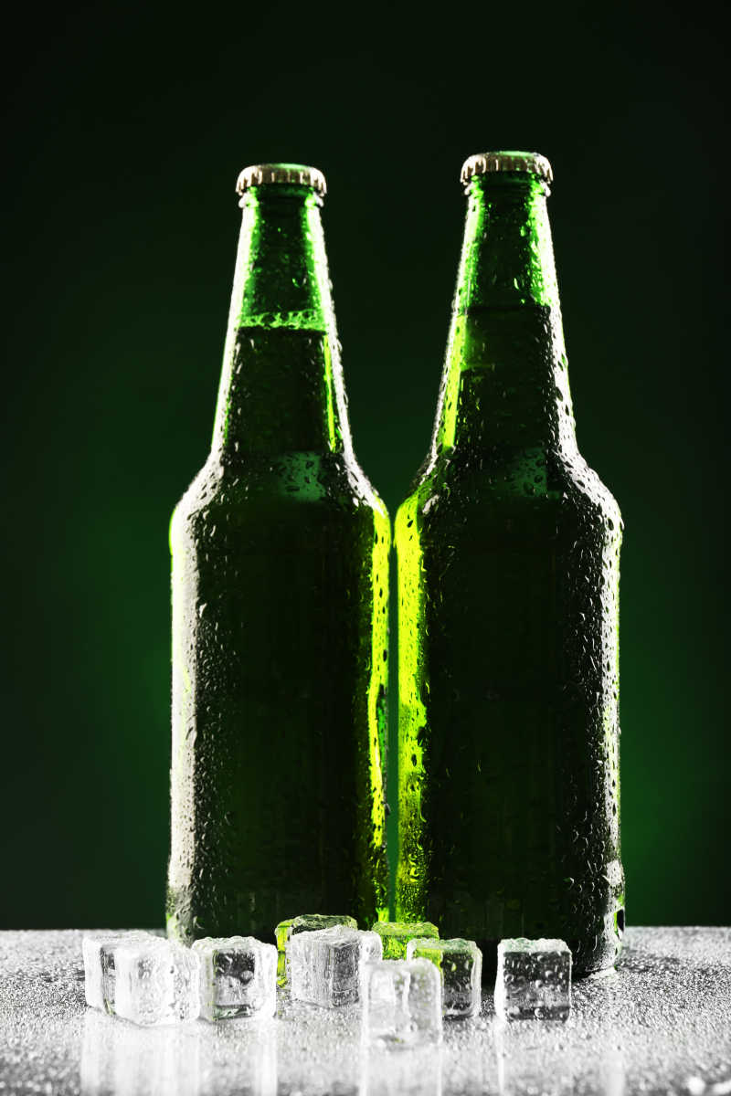 深绿色背景下带着水珠的酒瓶和冰块