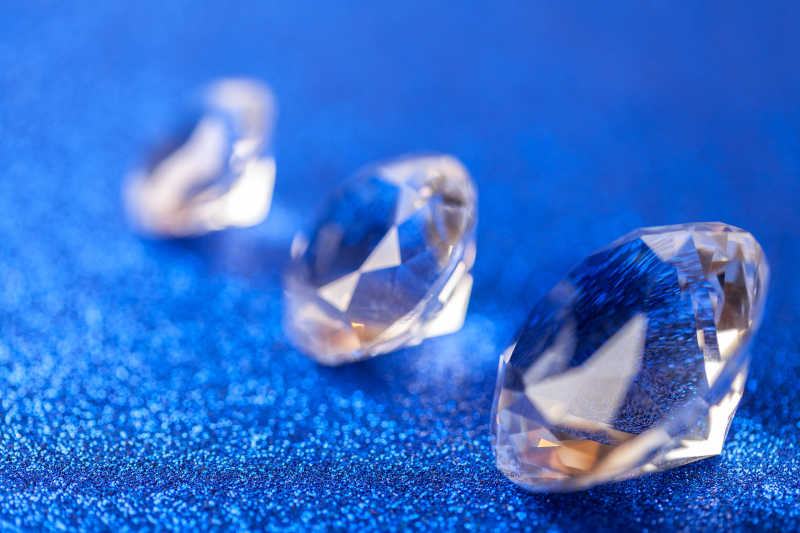 三大昂贵的钻石放在蓝色背景上闪闪发光的亮片的对角线