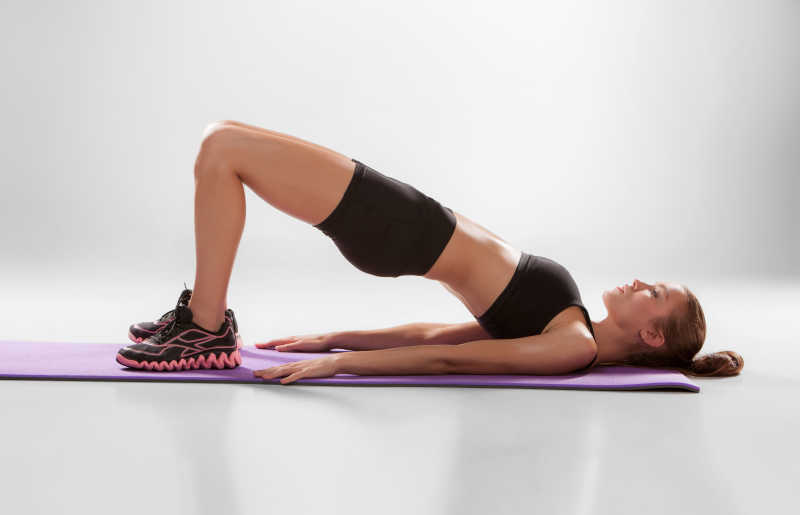 漂亮女人在灰色背景的淡紫色垫子上做健身运动