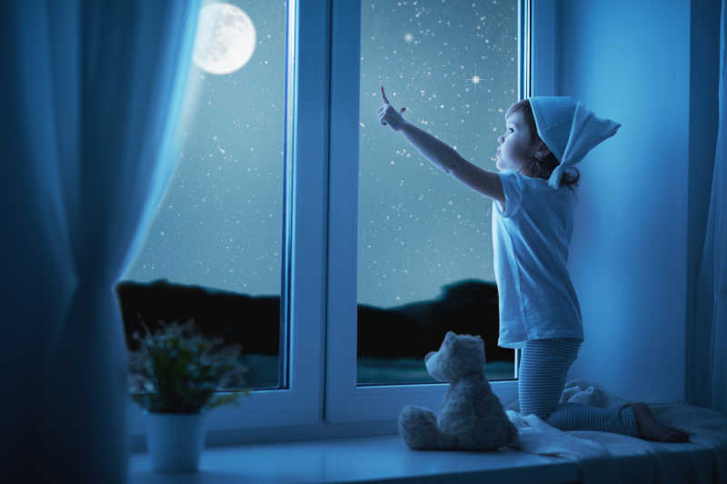 趴在窗户上看着夜空的小女孩
