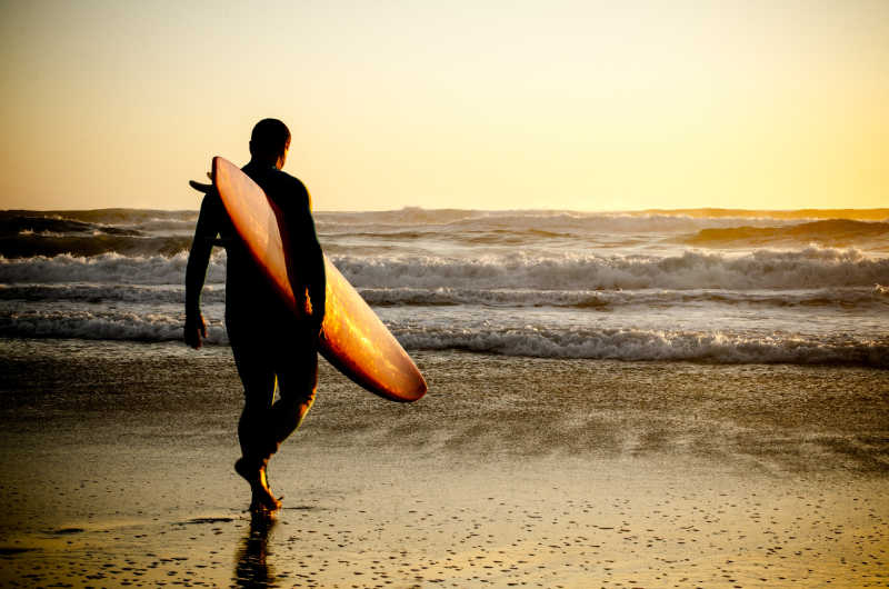 日落下拿着冲浪板走向海边的男人