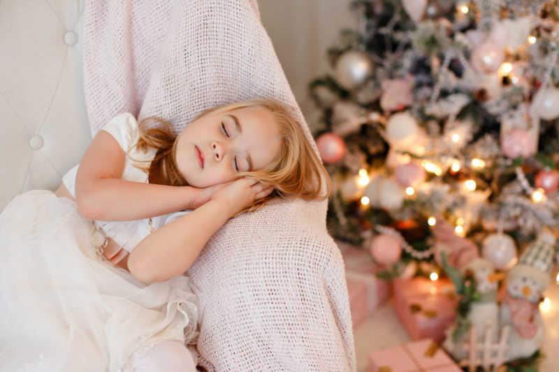 圣诞节礼物背景下睡着的穿着白色的连衣裙的小女孩
