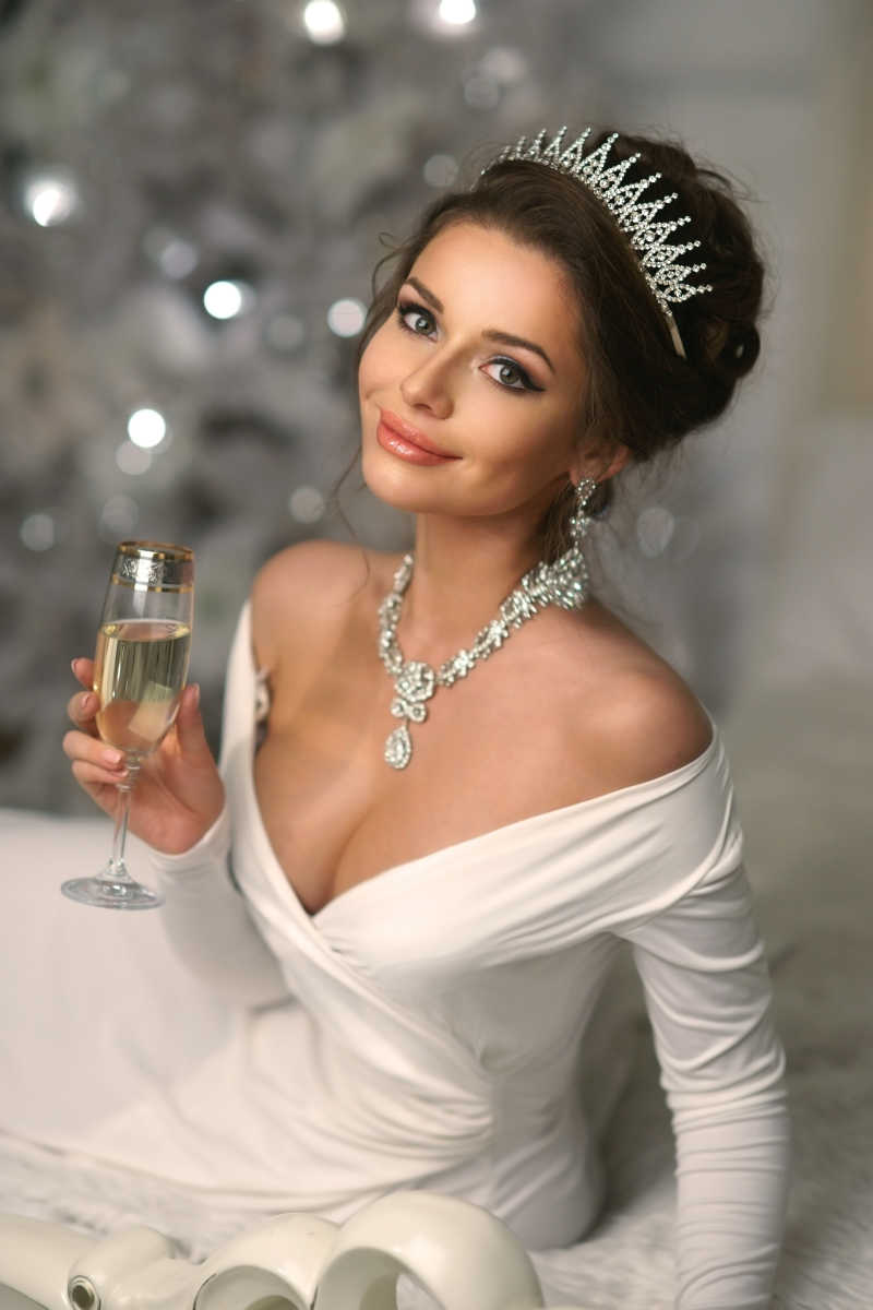 女士穿着白色晚礼服和珠宝首饰手里端着高脚玻璃杯香槟酒