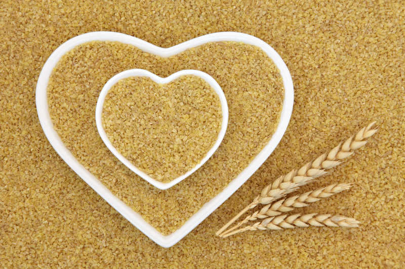 碾碎的干小麦超级食品与小麦叶鞘形成背景的心形碗
