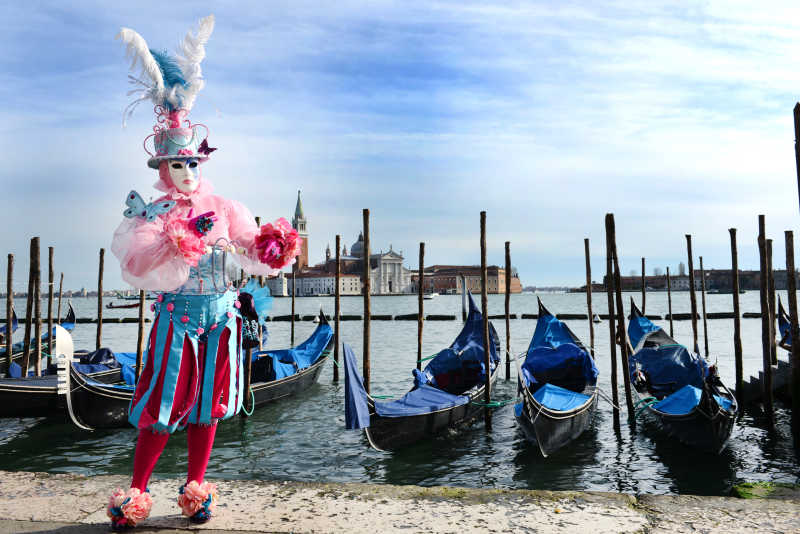 蓝天下停留在海边的小船和威尼斯狂欢节服装摄影