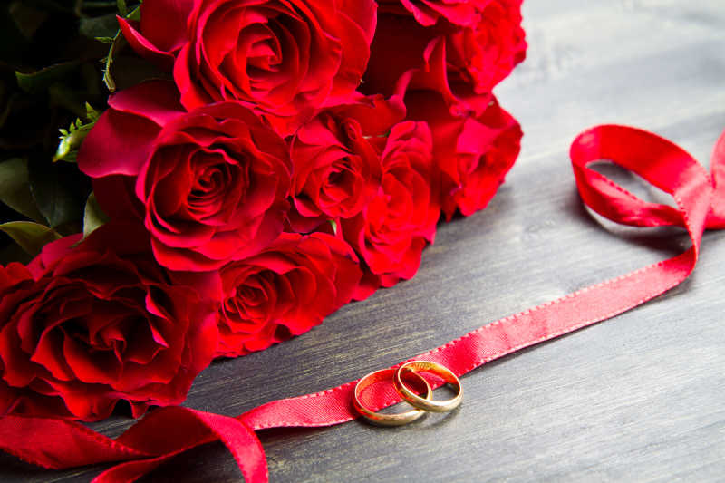木桌上的玫瑰花束和红丝带上的戒指