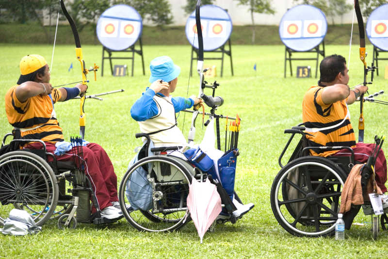 三个坐在轮椅上的残疾人比赛射箭