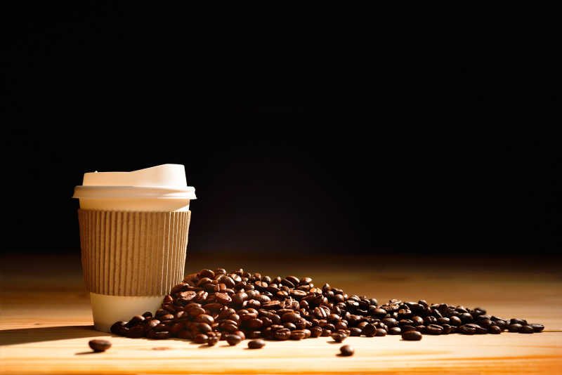 黑色背景下木桌上的咖啡杯和咖啡豆