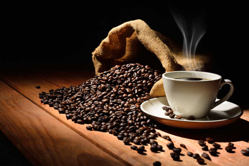 旧木桌上咖啡杯里热咖啡和咖啡豆
