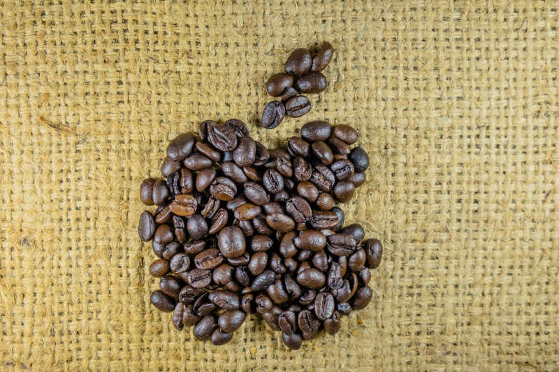 黄色亚麻布上咖啡豆组成的苹果商标造型
