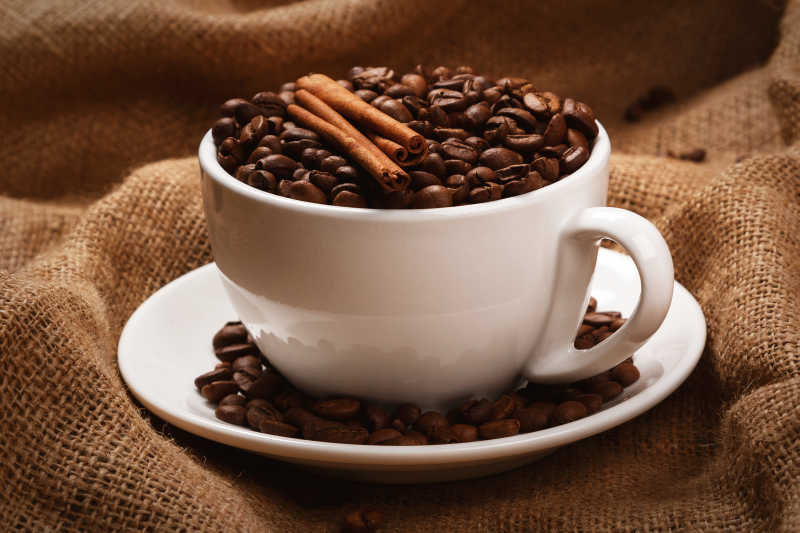 深色亚麻布上白色咖啡杯子里的咖啡豆和调味料