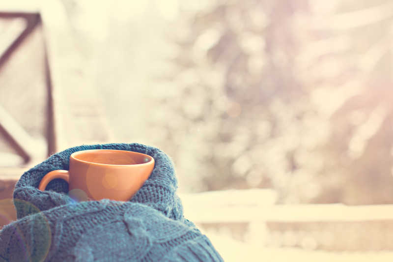 冬季有阳光的户外背景下蓝色针织衫包着的杯子