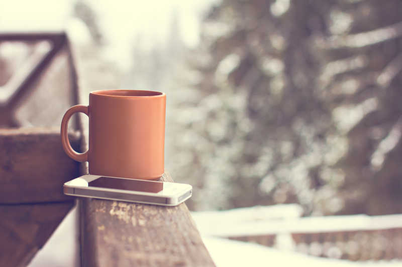 冬季有雪的室外背景下木围栏上的手机和杯子