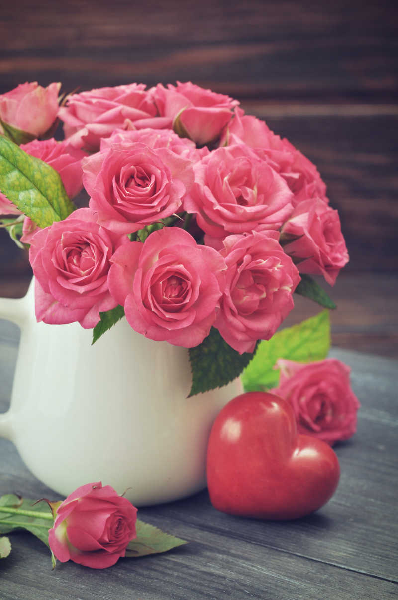 木制桌面上白色花瓶里的一束粉色玫瑰花