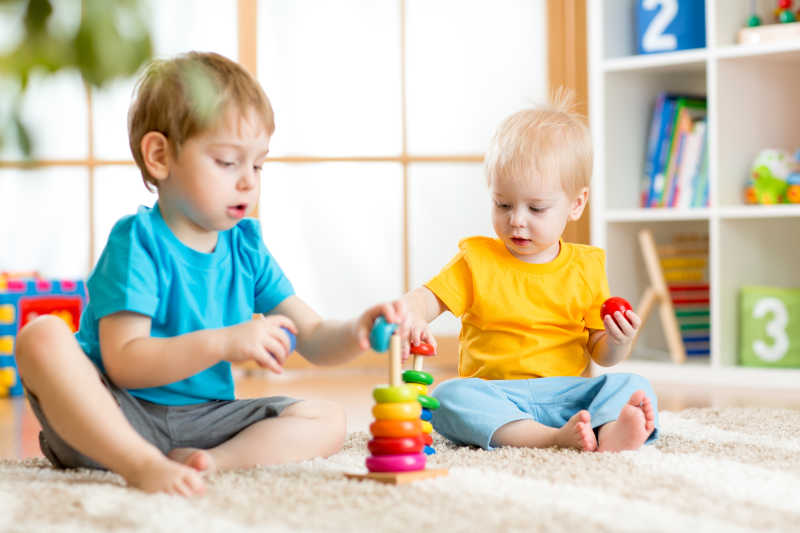 两个孩子坐在幼儿园的地摊上玩金字塔的游戏