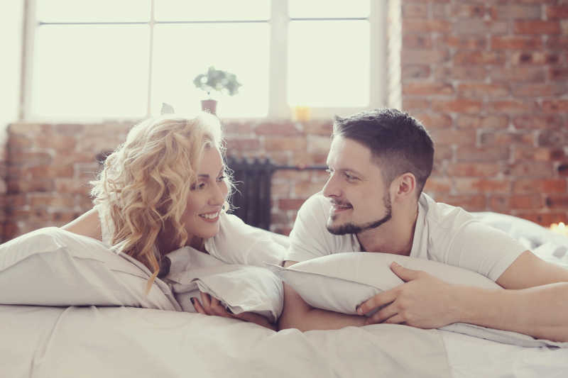 年轻美丽的夫妇在床上趴着相互对视