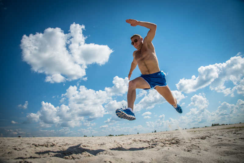 穿着蓝色短裤在海滩跑步的男人