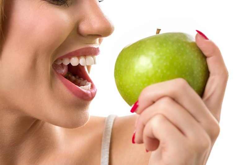 女性健康的牙齿咬绿色苹果