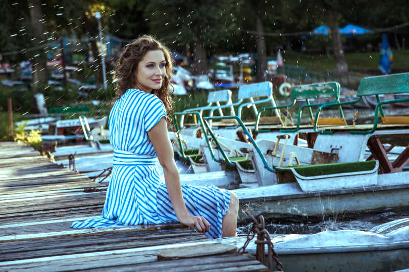 脸上有淡蓝色条纹的衣服和时尚化妆和发型坐在码头附近的金属银舟湖上的雀斑漂亮的年轻模特