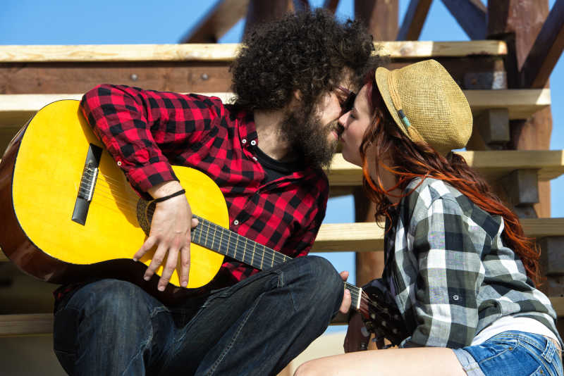 年轻情侣在户外接吻男子抱着吉他